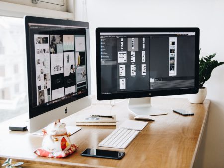 two imac s with keyboard and phones on desk